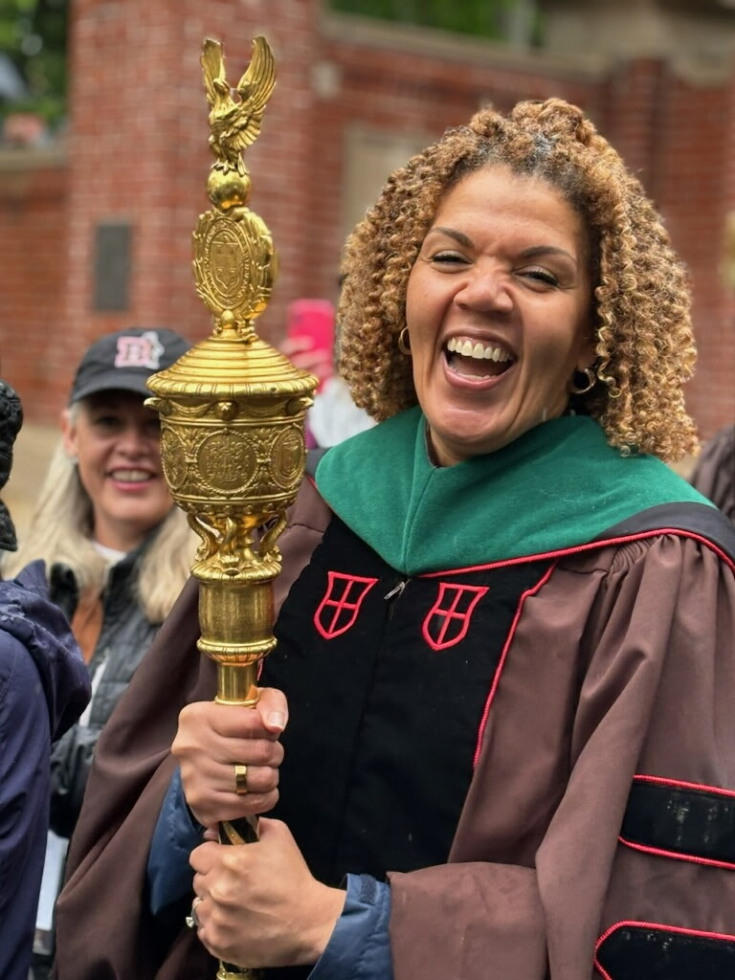 Vice President Patricia Poitevien smiling in a brown rode and green stole holding a scepter at Commencement 2026