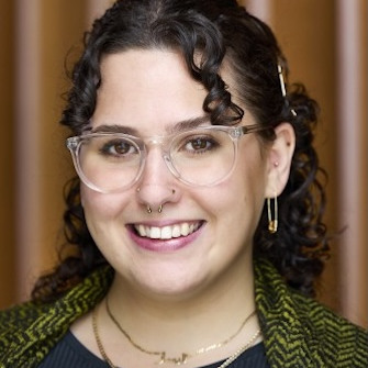 Smiling person with curly hair and glasses
