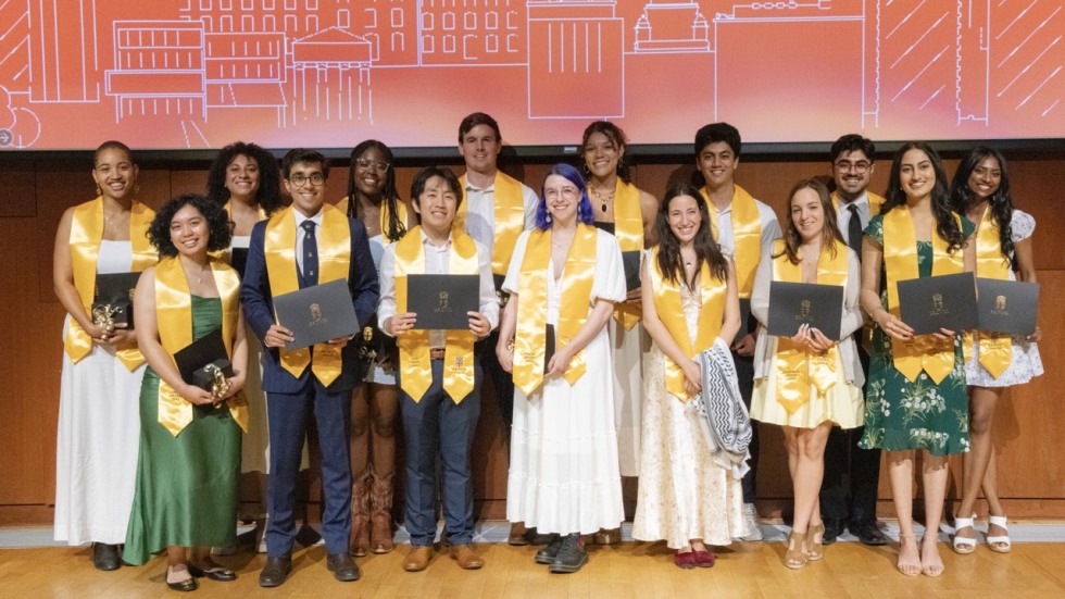 The 2024 Joslin Award winners are shown standing in a line, wearing their bright yellow Joslin recipient stoles, before a red backdrop featuring a white outline of the Brown campus skyline.