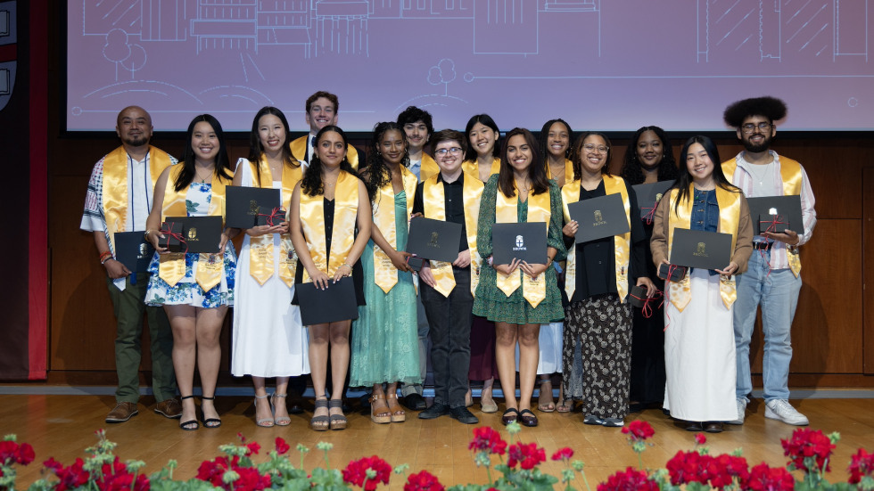The 2025 Campus Life Award winners are shown standing in a line, wearing their bright yellow Joslin recipient stoles, before a red backdrop featuring a white outline of the Brown campus skyline.
