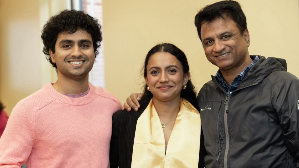 A Joslin Award winner with long, dark brown hair smiles next to two family members. One family member is wearing a pink sweater, and the other family member is wearing a black jacket.